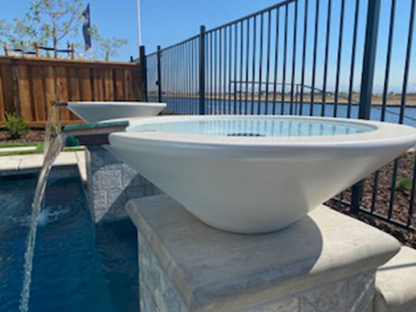 A close-up of a modern poolside water feature with a sleek white bowl cascading water into the pool