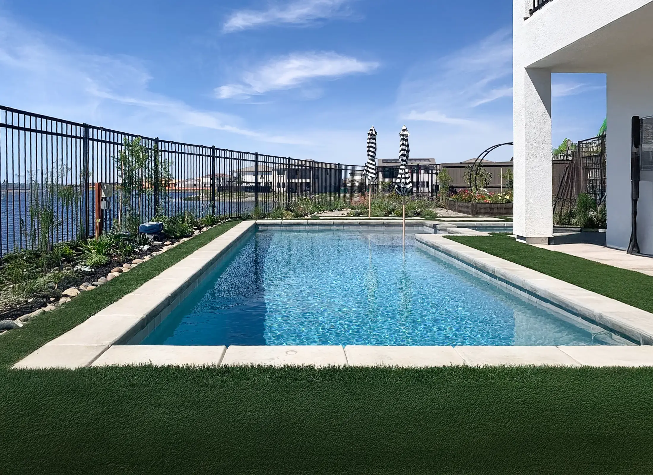 Rectangular backyard swimming pool with artificial turf, light stone coping, and a lakeside view.